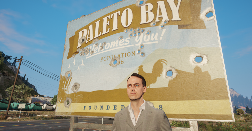 Jack Feebs standing in front of the bullet-riddled Paleto Bay welcome sign