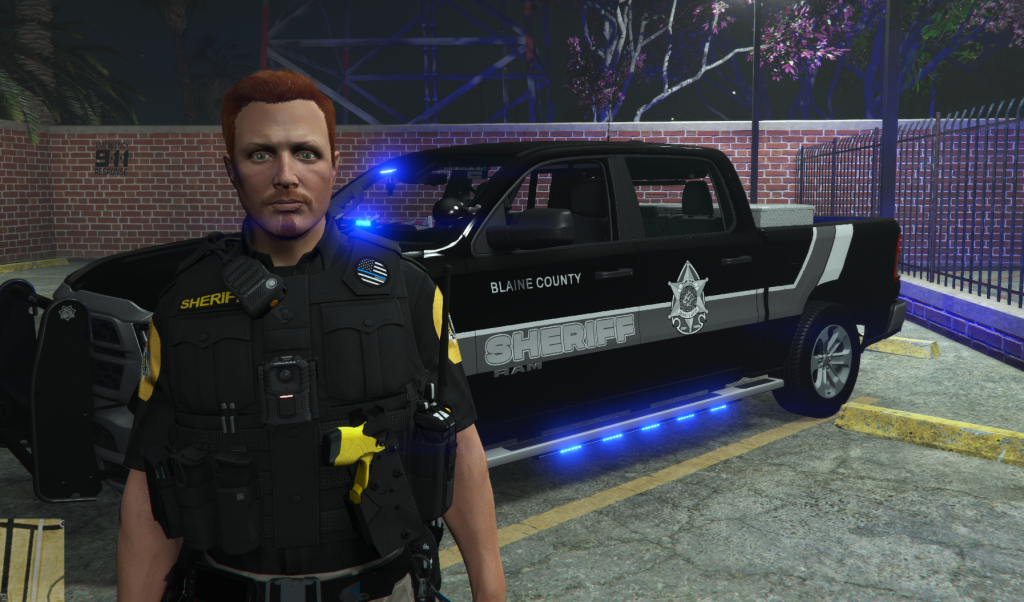 Wade Belson in Blaine County Sheriff uniform beside a patrol truck
