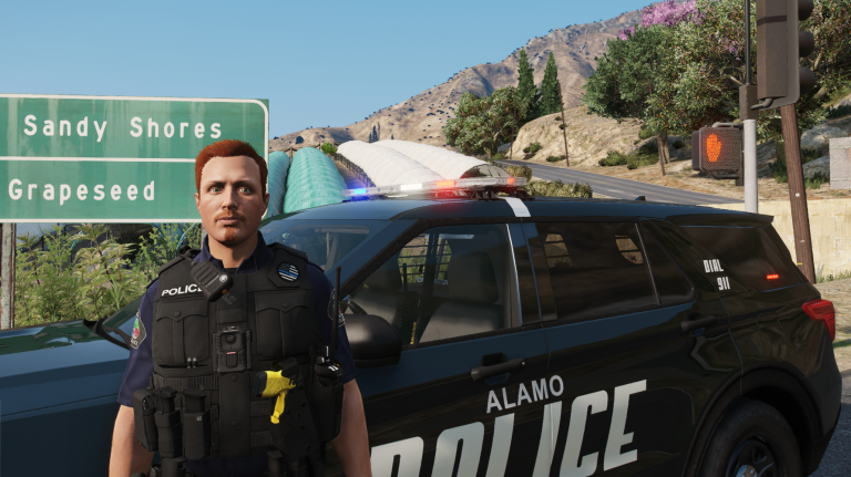 Wade Belson in Alamo PD uniform beside a patrol car at the Sandy Shores turnoff